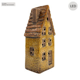 Side angle view of the Cello Tales from the Village Clockmaker’s Haven light-up ceramic house with warm LED glow illuminating the windows.