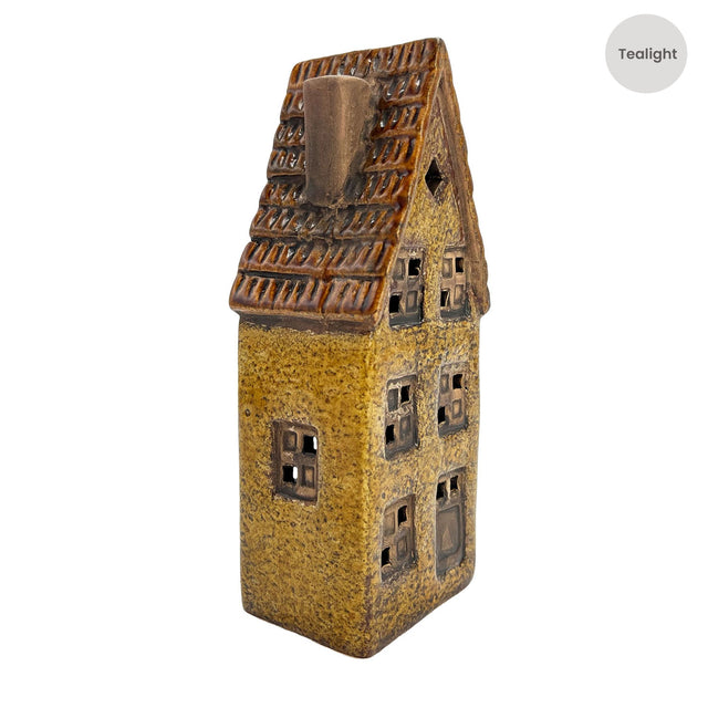 Side angle of the Cello Tales from the Village Clockmaker’s Haven tealight holder showing warm candlelight glowing through detailed windows.