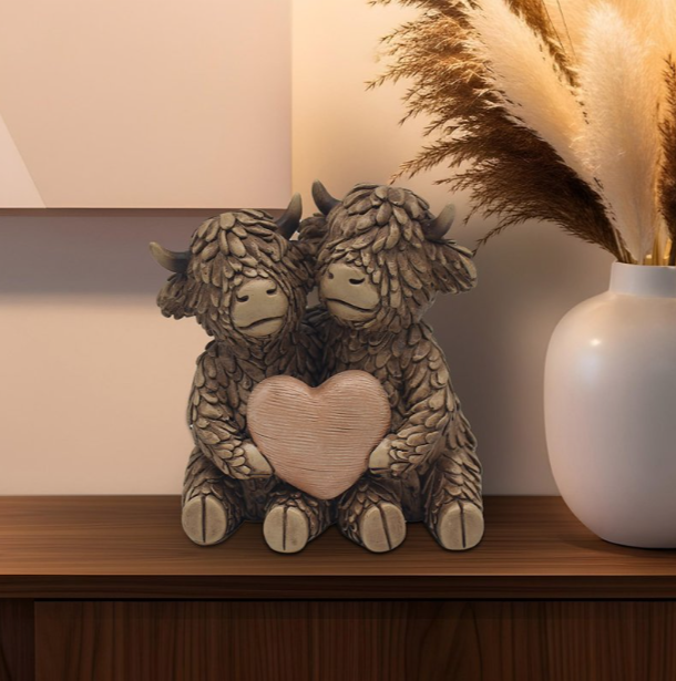 Resin Highland Cows holding heart ornament displayed on a sideboard with rustic décor, adding warmth and countryside charm to the living room.