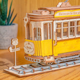 Wooden ROBOTIME Rolife kits Tramcar on a wooden surface with a blurred plant in the background