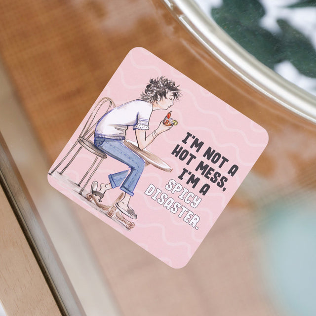 Pink square drinks coasters with an illustration of a person sitting on a chair and text, placed on a glass surface.