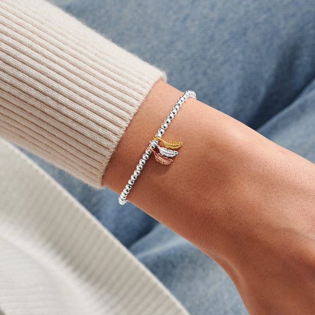 Mixed metal feather charm bracelet worn on wrist
