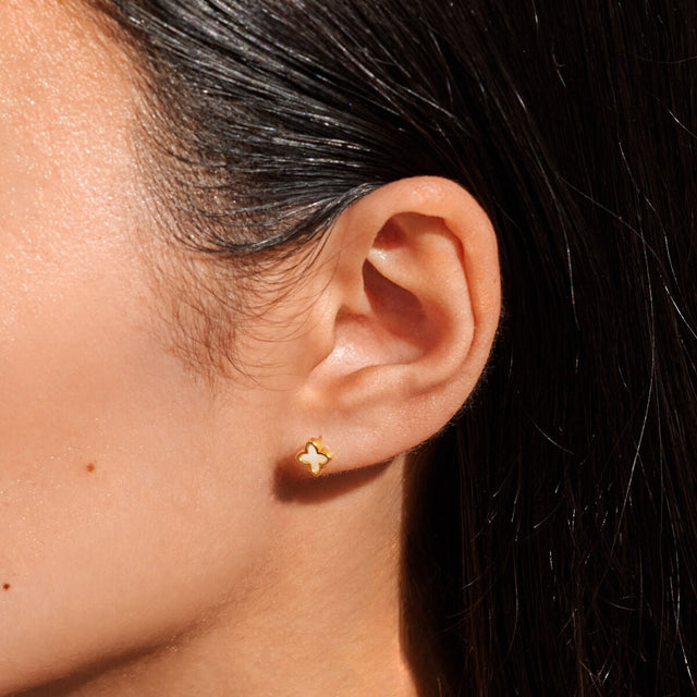 Woman wearing gold clover earrings with mother of pearl detail