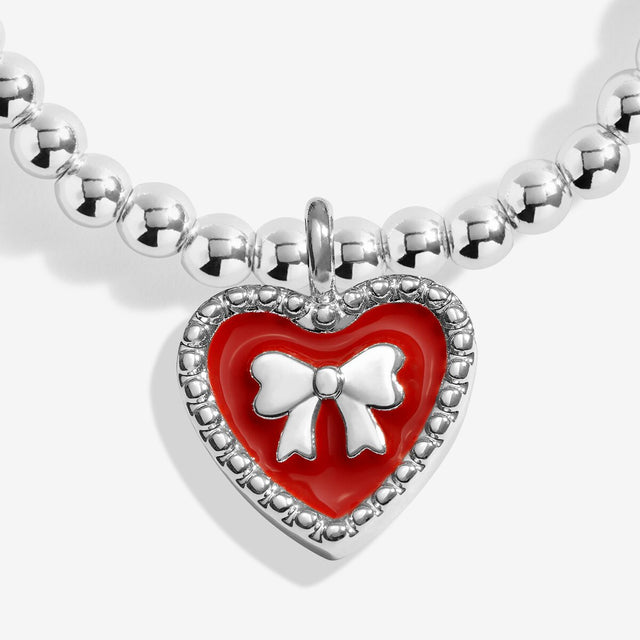 Close-up of the red heart charm with a silver-coloured bow on Joma Jewellery's Merry Christmas Granddaughter kids' bracelet