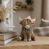 Lesser and Pavey Highland cow ornament with pink bow displayed on a shelf