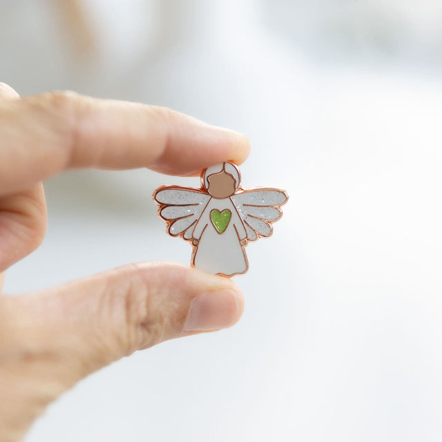 Hand holding the Splosh Angel of Healing pin, showing fine detailing and rose gold trim.