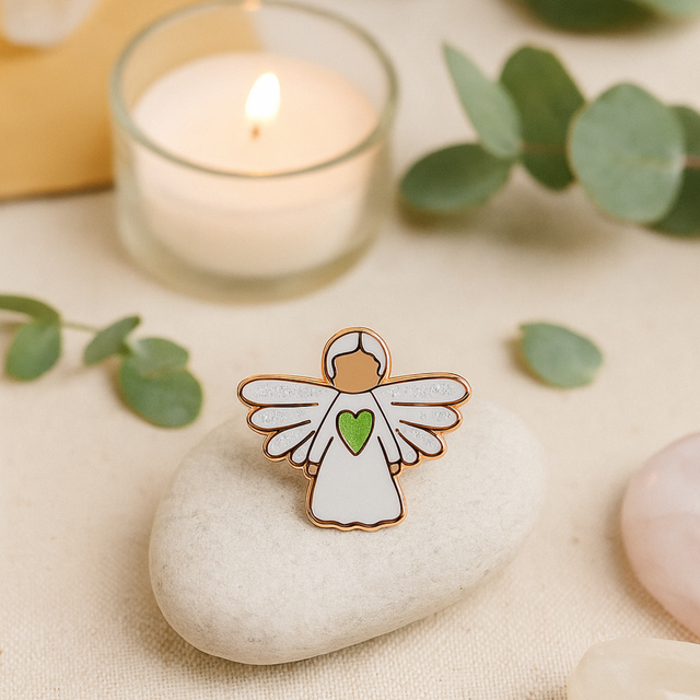 Angel of Healing guardian angel pin displayed beside a glowing candle and natural stones, symbolising calm and peace.
