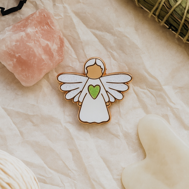 Splosh Angel of Healing pin resting on a soft white fabric surface, highlighting elegant rose gold and ceramic design.