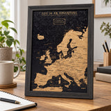 Splosh black Europe travel map with black frame standing on wooden furniture in a neutral home setting