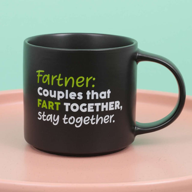Close-up of Splosh Cheeky Mug Fartner quote design, black witty ceramic coffee cup with bold green and white lettering for couples.