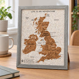 Splosh grey UK & Ireland travel map with grey woodgrain frame, compact map standing on a desk beside a mug