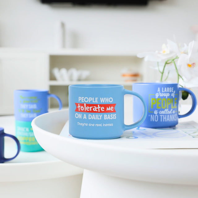 Splosh Cheeky Mug Tolerate on kitchen table, humorous blue mug with cheeky quote, funny novelty coffee cup for home or office use.