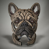 A sculpture of a French Bulldog with a fawn-colored head and a textured, wooden-like body, set against a black background.